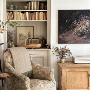 A beautiful vintage home, featuring an arm chair, bookcase, flowers and artwork. 