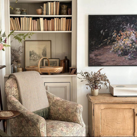 A beautiful vintage home, featuring an arm chair, bookcase, flowers and artwork. 