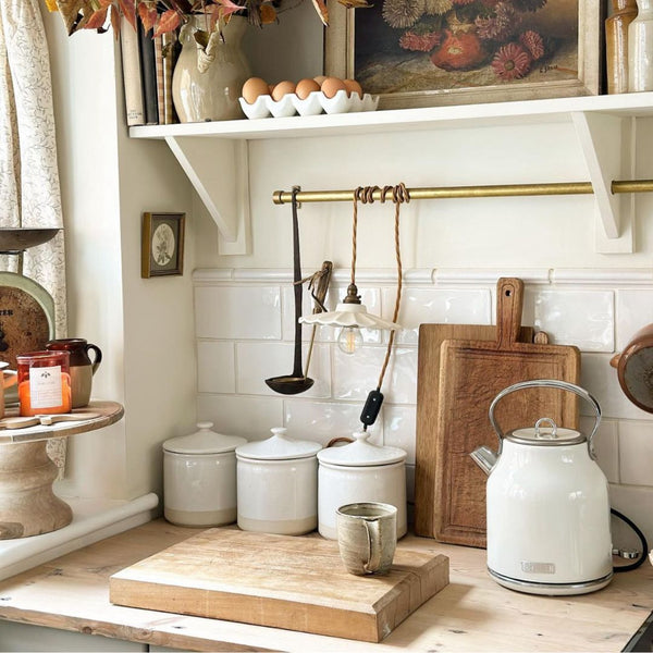 A vintage kitchen, featuring a vintage kettle, tea, sugar and teabag holders, alongside candles and artwork. 