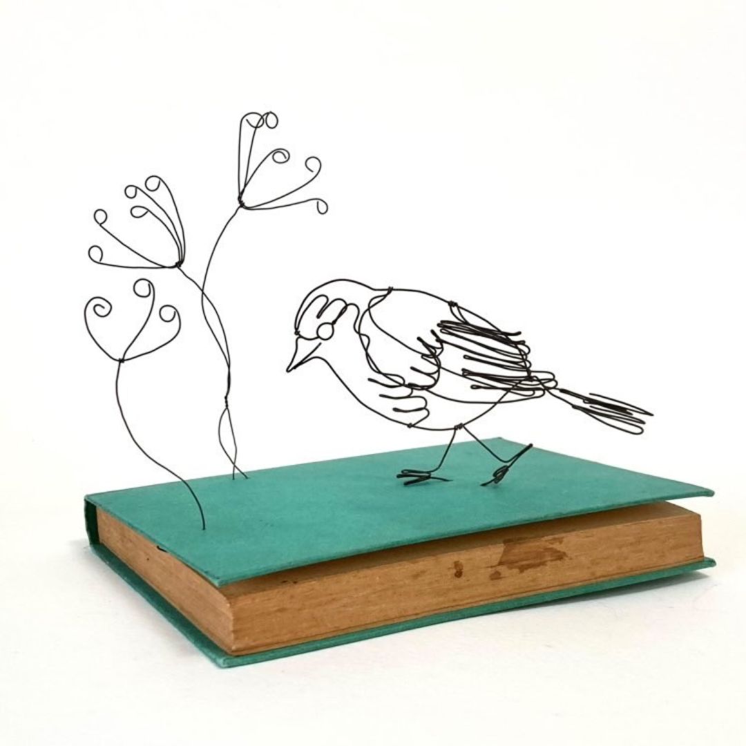 A wire robin, beautifully crafted at the Pod & Pip workshop, perched on top of a book