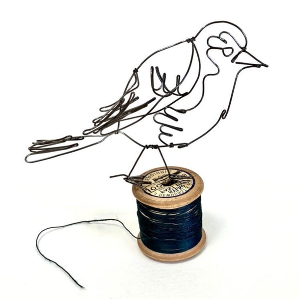 A wire robin, beautifully crafted at the Pod & Pip workshop, perched on top of a reel of wire